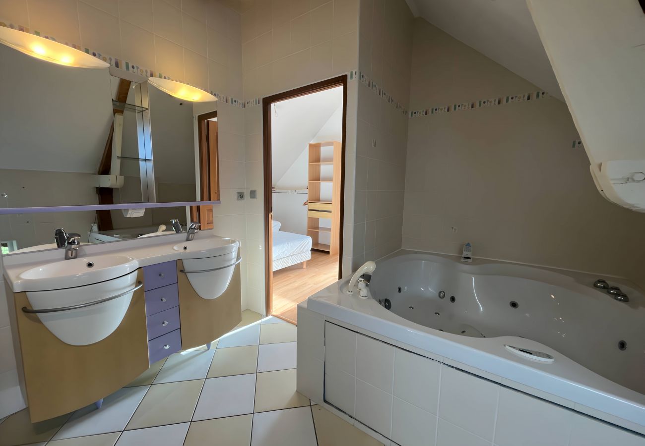 Salle de bain entièrement carrelée avec baignoire d'angle balnéo, double lavabos confortables avec vasque et miroirs